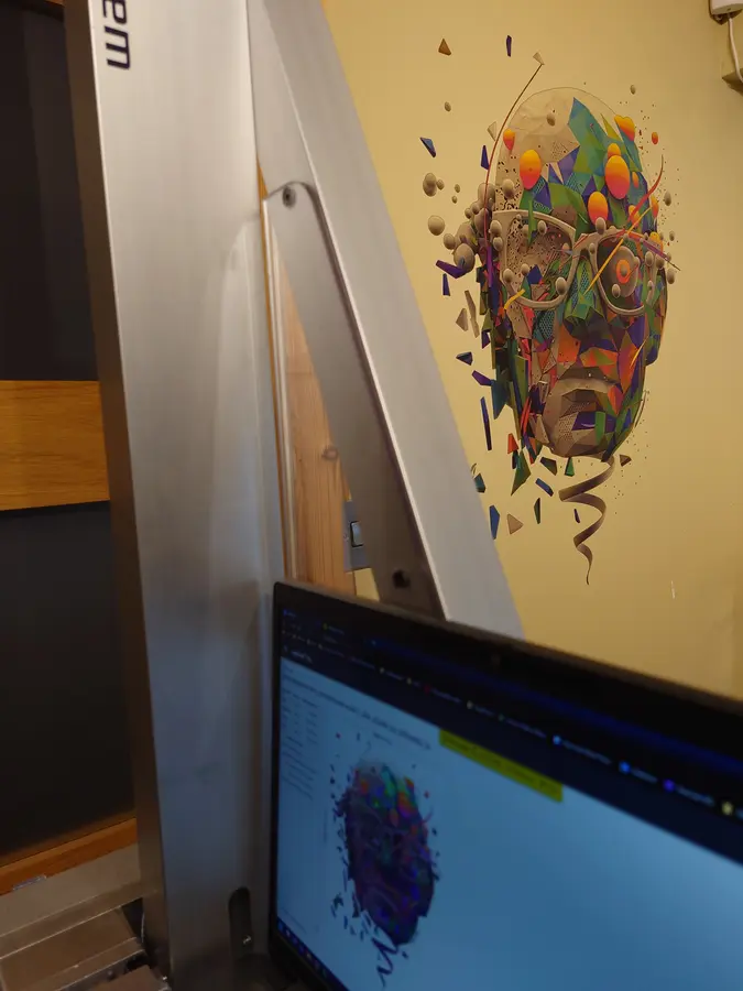Wanddrucker vor Ort beim Druck eines bunten Motivs, davor der Laptop mit der Druckvorlage